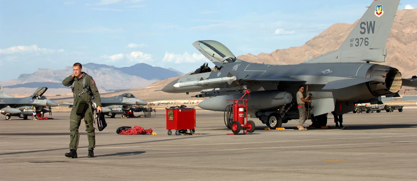 A U.S. Air Force pilot walks away from a grounded F-16 fighter jet on a desert flight line — a visual metaphor for the Magnificent 7 coming back to earth.